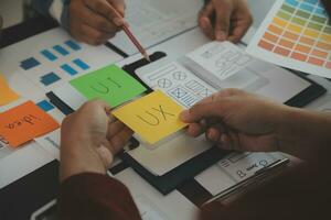 Close up ux developer and ui designer brainstorming about mobile app interface wireframe design on table with customer breif and color code at modern office.Creative digital development agency photo