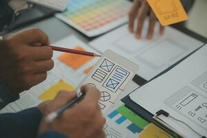 Close up ux developer and ui designer brainstorming about mobile app interface wireframe design on table with customer breif and color code at modern office.Creative digital development agency photo