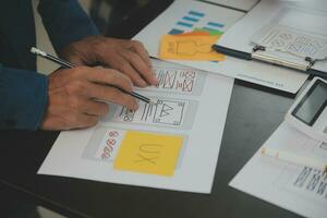 Close up ux developer and ui designer brainstorming about mobile app interface wireframe design on table with customer breif and color code at modern office.Creative digital development agency photo