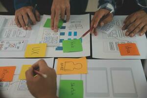 Close up ux developer and ui designer brainstorming about mobile app interface wireframe design on table with customer breif and color code at modern office.Creative digital development agency photo