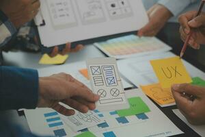 Close up ux developer and ui designer brainstorming about mobile app interface wireframe design on table with customer breif and color code at modern office.Creative digital development agency photo