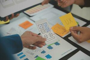 Close up ux developer and ui designer brainstorming about mobile app interface wireframe design on table with customer breif and color code at modern office.Creative digital development agency photo