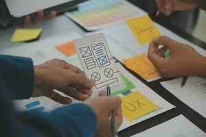 Close up ux developer and ui designer brainstorming about mobile app interface wireframe design on table with customer breif and color code at modern office.Creative digital development agency photo