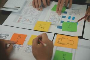 Close up ux developer and ui designer brainstorming about mobile app interface wireframe design on table with customer breif and color code at modern office.Creative digital development agency photo