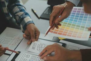 Close up ux developer and ui designer brainstorming about mobile app interface wireframe design on table with customer breif and color code at modern office.Creative digital development agency photo