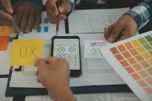 Close up ux developer and ui designer brainstorming about mobile app interface wireframe design on table with customer breif and color code at modern office.Creative digital development agency photo