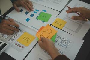 Close up ux developer and ui designer brainstorming about mobile app interface wireframe design on table with customer breif and color code at modern office.Creative digital development agency photo