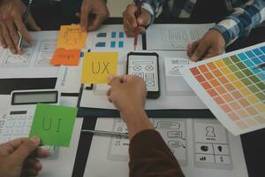 Close up ux developer and ui designer brainstorming about mobile app interface wireframe design on table with customer breif and color code at modern office.Creative digital development agency photo