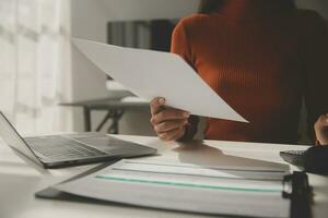 Asian Businesswoman Using laptop computer and working at office with calculator document on desk, doing planning analyzing the financial report, business plan investment, finance analysis concept. photo