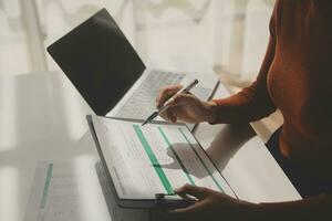 Asian Businesswoman Using laptop computer and working at office with calculator document on desk, doing planning analyzing the financial report, business plan investment, finance analysis concept. photo