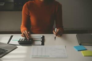 mujer de negocios asiática que usa una computadora portátil y trabaja en la oficina con un documento de calculadora en el escritorio, planificando el análisis del informe financiero, la inversión del plan de negocios, el concepto de análisis financiero. foto