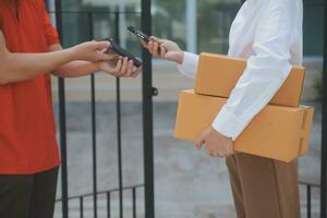 asiático mujer recepción producto desde entrega hombre a hogar, joven propietario mujer orden producto desde teléfono inteligente solicitud, mujer con en línea negocio o SME concepto. foto