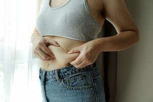 Close up of a belly with scar from c-section and abdominal fat. Women's health. A woman dressed up in sportswear demonstrating her imperfect body after a childbirth with nursery on the background. photo