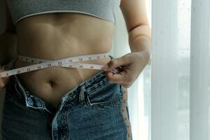 Close up of a belly with scar from c-section and abdominal fat. Women's health. A woman dressed up in sportswear demonstrating her imperfect body after a childbirth with nursery on the background. photo