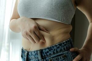 Close up of a belly with scar from c-section and abdominal fat. Women's health. A woman dressed up in sportswear demonstrating her imperfect body after a childbirth with nursery on the background. photo