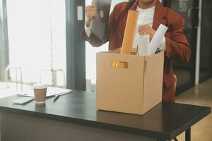 Business man employee stressful resignation from job while picking up personal belongings into brown cardboard box and carrying to walking out from office photo