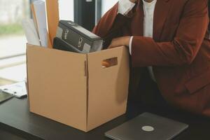 Business man employee stressful resignation from job while picking up personal belongings into brown cardboard box and carrying to walking out from office photo