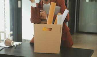 Business man employee stressful resignation from job while picking up personal belongings into brown cardboard box and carrying to walking out from office photo