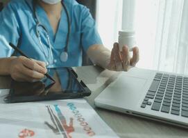 del doctor trabajando en ordenador portátil computadora, escritura prescripción portapapeles con grabar información papel carpetas en escritorio en hospital o clínica, cuidado de la salud y médico concepto. atención en estetoscopio foto