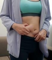 un mujer muestra un inflado grueso barriga, el concepto de exceso peso y peso pérdida foto