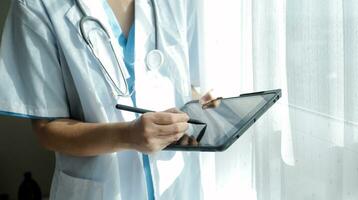 Female Doctor Wearing Scrubs In Hospital Corridor Using Digital Tablet photo