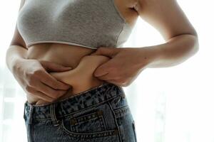 Close up of a belly with scar from c-section and abdominal fat. Women's health. A woman dressed up in sportswear demonstrating her imperfect body after a childbirth with nursery on the background. photo