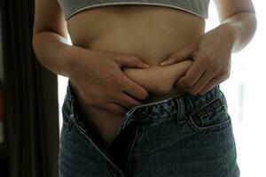 Close up of a belly with scar from c-section and abdominal fat. Women's health. A woman dressed up in sportswear demonstrating her imperfect body after a childbirth with nursery on the background. photo