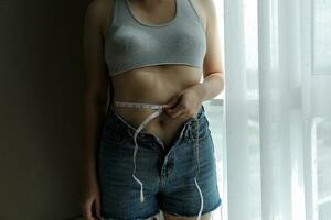 Close up of a belly with scar from c-section and abdominal fat. Women's health. A woman dressed up in sportswear demonstrating her imperfect body after a childbirth with nursery on the background. photo
