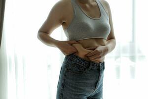 Close up of a belly with scar from c-section and abdominal fat. Women's health. A woman dressed up in sportswear demonstrating her imperfect body after a childbirth with nursery on the background. photo