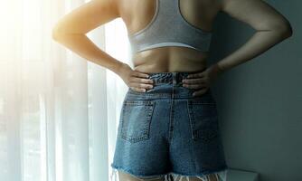 Close up of a belly with scar from c-section and abdominal fat. Women's health. A woman dressed up in sportswear demonstrating her imperfect body after a childbirth with nursery on the background. photo