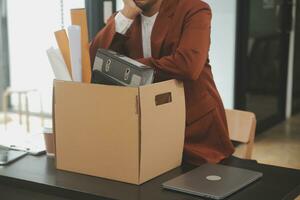 Business man employee stressful resignation from job while picking up personal belongings into brown cardboard box and carrying to walking out from office photo