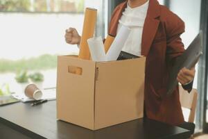 Business man employee stressful resignation from job while picking up personal belongings into brown cardboard box and carrying to walking out from office photo