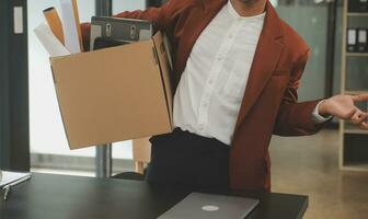 Business man employee stressful resignation from job while picking up personal belongings into brown cardboard box and carrying to walking out from office photo