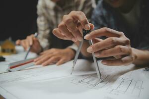 Team of multiethnic architects working on construction plans in meeting room. Engineers discussing on project in office. Mature businessman and woman standing around table working on blueprint. photo