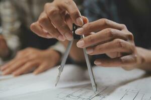 Team of multiethnic architects working on construction plans in meeting room. Engineers discussing on project in office. Mature businessman and woman standing around table working on blueprint. photo