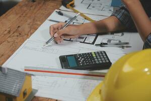 equipo de multiétnico arquitectos trabajando en construcción planes en reunión habitación. ingenieros que se discute en proyecto en oficina. maduro empresario y mujer en pie alrededor mesa trabajando en Plano. foto