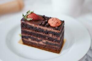 Piece of chocolate cake with strawberries and macaroons on white plate photo