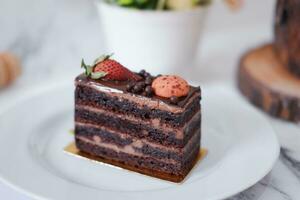 Piece of chocolate cake with strawberries and macaroons on white plate photo