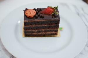 Piece of chocolate cake with strawberries and macaroons on white plate photo