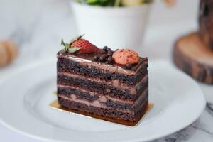 Piece of chocolate cake with strawberries and macaroons on white plate photo