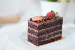 Piece of chocolate cake with strawberries and macaroons on white plate photo