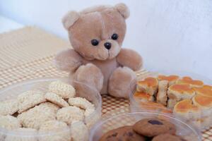 Teddy bear and cookies in plastic box on wooden table background. photo