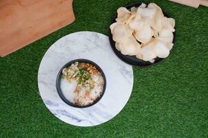 Rice porridge with chicken in white plate on green grass background photo