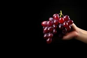 Hand holding a bunch of red grapes isolated on a black background with copy space. ai generated photo