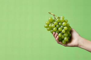 Hand holding green grapes bunch isolated on green background with copy space. ai generated photo
