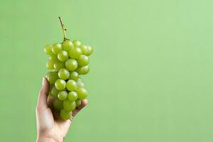 Hand holding green grapes bunch isolated on green background with copy space. ai generated photo