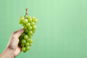 Hand holding green grapes bunch isolated on green background with copy space. ai generated photo