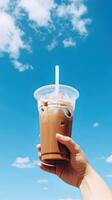mano participación con hielo café en un el plastico taza con un azul cielo y nube antecedentes. ai generado foto