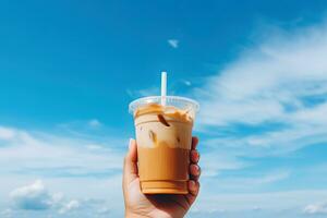 Hand holding iced coffee in a plastic cup with a blue sky and cloud background. ai generated photo