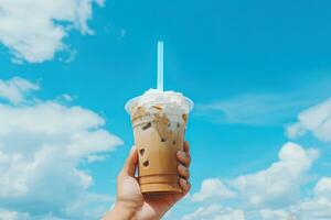 Hand holding iced coffee in a plastic cup with a blue sky and cloud background. ai generated photo